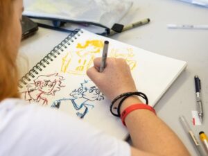 student sketching in a sketchbook from over their shoulder