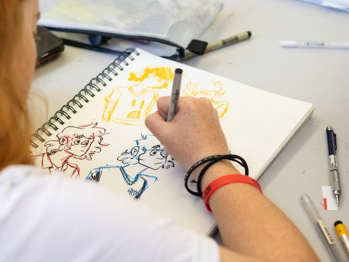 student sketching in a sketchbook from over their shoulder