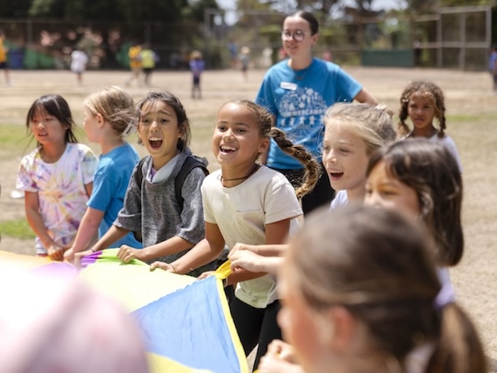 kids and a counselor playing with a giant parachute in a field