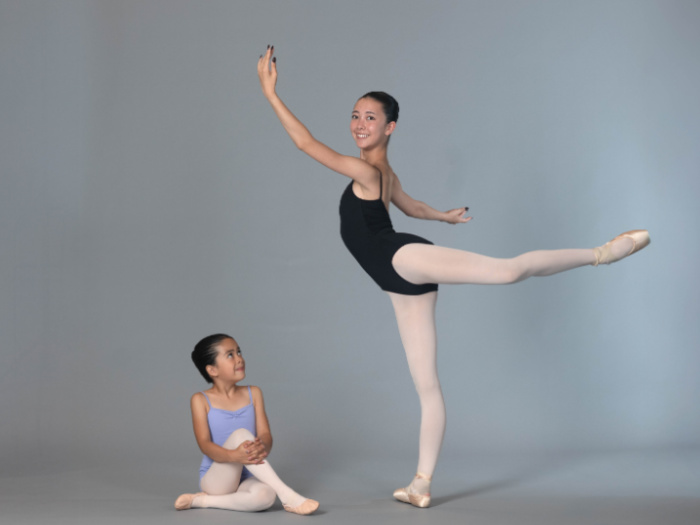 two ballerinas one small seated and one taller doing a complex ballet move