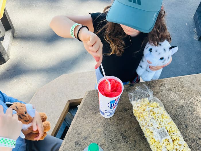 girl eating red slushie with spoon holding white tiger stuffie
