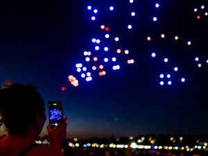 drone show of confetti emoji in sky with person taking a photo on their phone