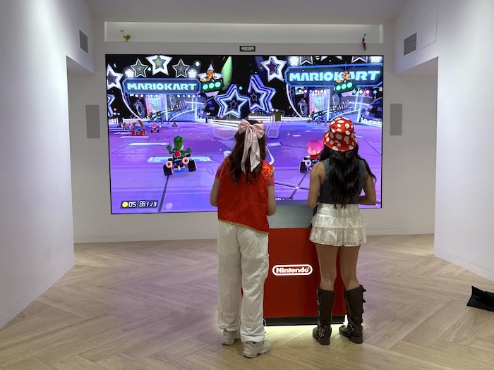 two players playing nintendo mario kart on a big screen in a store