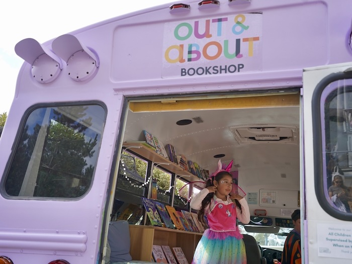 child dressed as rainbow unicorn inside a mobile pride book bus