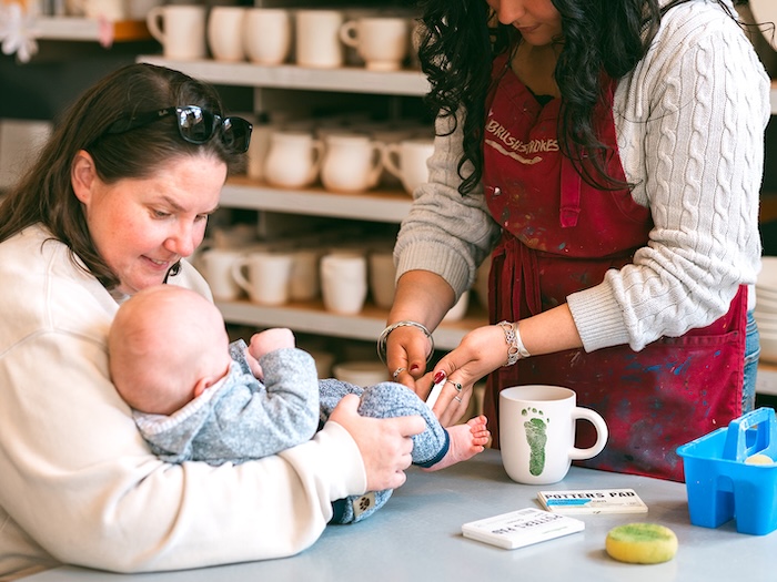 baby getting footprints stamped onto a tile or mug at brushstrokes