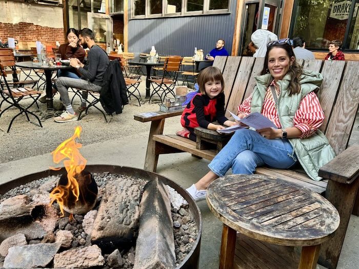 adult and child reading at the fire pit of drake's patio seating