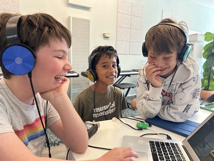 three kids in headphones and laptop making music or recording a podcast