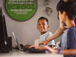 student at a computer with a teacher and second student looking on