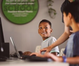 student at a computer with a teacher and second student looking on