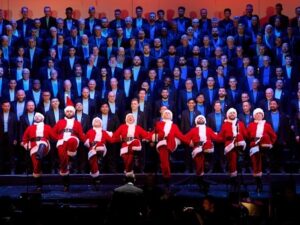 San Francisco Gay Men’s Chorus performing on risers with a row of santa clauses up front