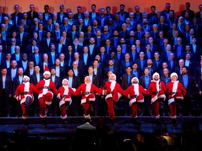 San Francisco Gay Men’s Chorus performing on risers with a row of santa clauses up front