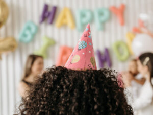 wearing birthday party pink hat on head facing a birthday party
