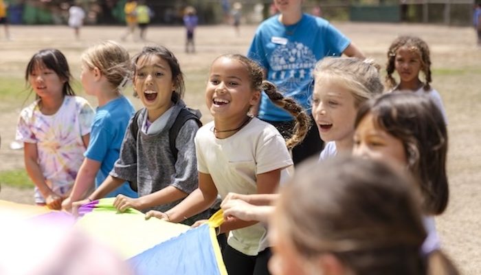 kids and a counselor playing with a giant parachute in a field