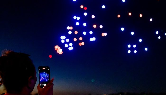 drone show of confetti emoji in sky with person taking a photo on their phone